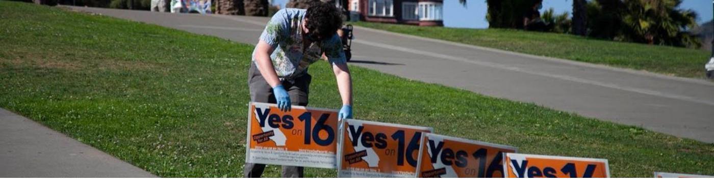 Sean placing Yes on 16 campaign signs along a park path